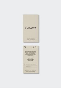 Deux étiquettes en coton durable beige avec un texte sur l'engagement à réduire les produits chimiques et à économiser l'eau dans la production de mode.