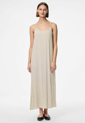 Maxi vestido de color beige claro con tirantes finos, hecho de una tela texturizada, con un silueta fluida que llega a mitad de pantorrilla. Se lleva con zapatos planos negros.