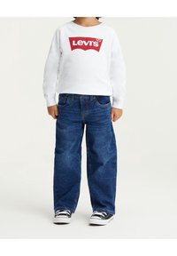 Vit sweatshirt med röd Levi's-logga, tillsammans med blå denimjeans. Skorna är svarta med vita sulor. Avslappnad, ledig passform.
