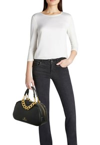 Borsa nera con dettagli a catena dorata, finitura testurizzata e chiusura con zip. Completa l'outfit una maglietta bianca a maniche lunghe e jeans scuri.