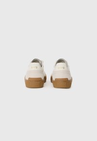Et par off-white sneakers med gummisåler, "1973" i gull på hælene, og "Pepe Jeans London" preget på baksiden av sålene.