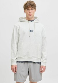 Jasnoszara bluza z kapturem, wykonana z miękkiego materiału, z przednią kieszenią, regulowanym kapturem i małym niebieskim logiem. Nosi ją osoba w ciemnej koszulce i szarych szortach.