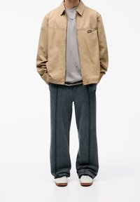 Chaqueta ligera beige, sudadera gris de cuello redondo, pantalones sueltos gris oscuro con costuras visibles, zapatillas blancas y una cadena de plata.