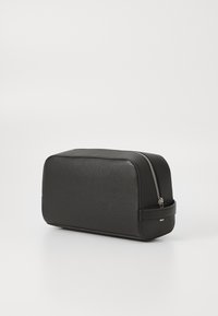 Trousse de toilette en cuir noir avec une surface texturée, de forme rectangulaire et avec une fermeture éclair en métal argenté. Équipée d'une poignée latérale pour un transport facile.