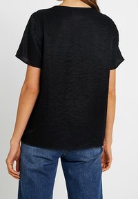 T-shirt noir à manches courtes, en tissu texturé, col rond, coupe décontractée, associé à un jean en denim bleu, montrant un tomber naturel.