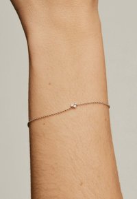 Pulsera de cadena de plata con un pequeño acento de piedras transparentes, mostrada en una muñeca. La cadena es delicada con una textura fina.