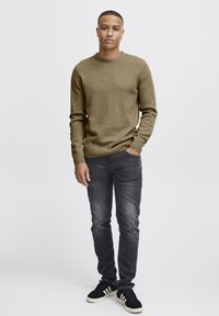 Olivenfarget strikkegenser med rund hals, sammen med mørkegrå slim-fit jeans og svarte sneakers med hvite detaljer. Enkel design.