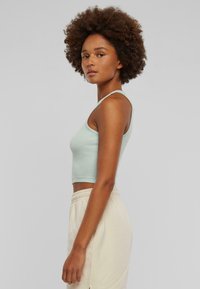 Light green ribbed crop top with thin straps, showcasing a fitted design. Worn with light beige, drawstring sweatpants.