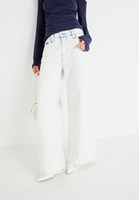 Jeans de denim de culoare albastru deschis, cu croială lărgră, talie înaltă, cusături contrastante și margini brut. Asortat cu un top ajustat, de culoare bleumarin, cu mânecă lungă.