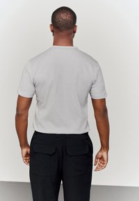 Vaaleanharmaa lyhythihainen paita pyöreällä pääntiellä, yhdistetty mustiin housuihin, joissa on kaksi takataskua. Sileä pinta, minimalistinen muotoilu.