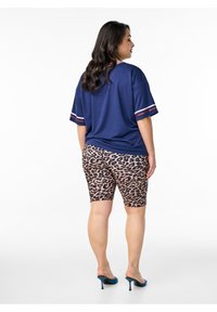 Granatowa koszulka oversize z paskami na rękawach w połączeniu z szortami rowerowymi w panterkę. Modelka nosi turkusowe buty na wysokim obcasie. Gładka tekstura tkaniny.
