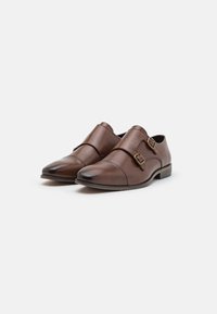 Zapatos de cuero marrón con diseño de doble hebilla, punteras puntiagudas y textura suave. Ligeros y con un pequeño tacón apilado.