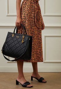Sac à main noir matelassé avec ferrures dorées, doté d'une poignée supérieure et d'une bandoulière. Assorti à une jupe imprimé léopard et des sandales noires à talons carrés.