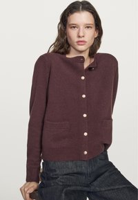 Maroon knit cardigan featuring a round neckline, five button closure, two front pockets, and ribbed cuffs. Soft texture, relaxed fit.