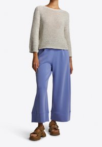 Lichtgrijs gebreide trui met een ronde hals, gecombineerd met losse lavendelkleurige wijde pijpen broek en bruine platformsandalen.