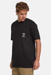 Camiseta de algodón negra con mangas cortas, que presenta un bolsillo en el frente y un gráfico de palmera blanca en el bolsillo. Parte trasera lisa.