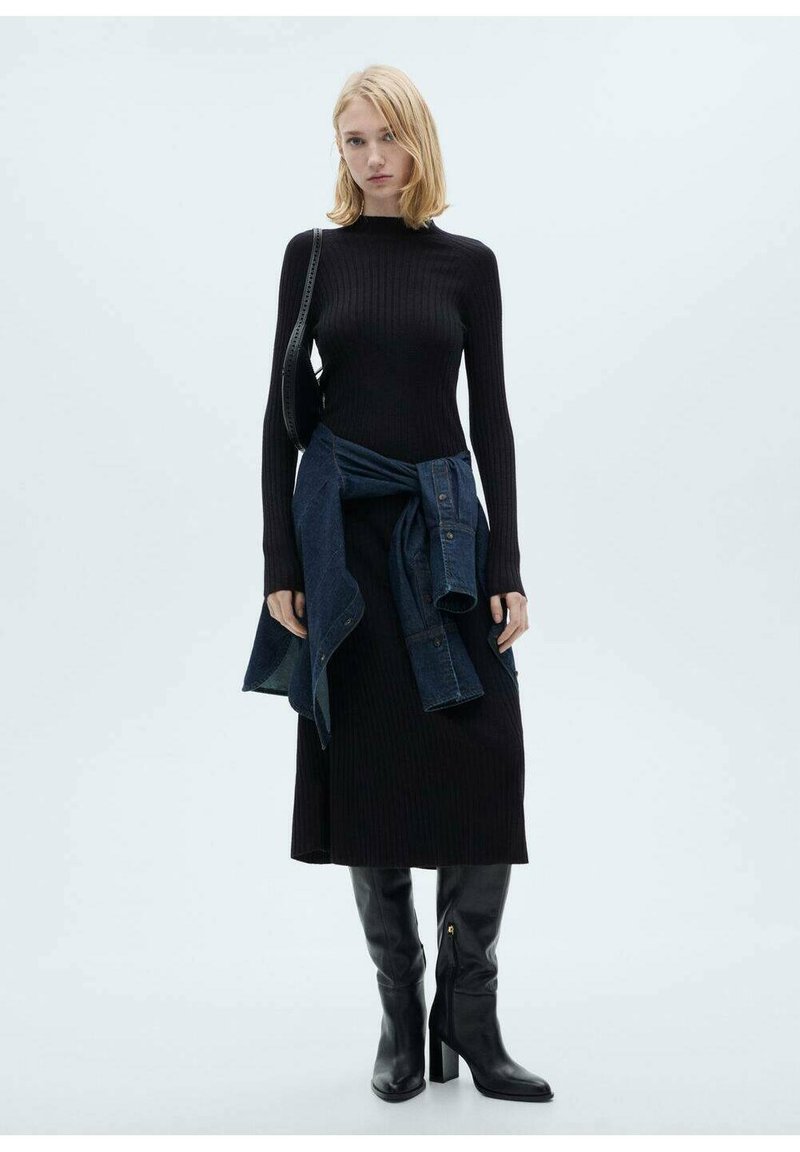Robe en tricot côtelé noire à manches longues, associée à une chemise en jean nouée à la taille. Des bottes noires lisses à talons hauts jusqu'aux genoux complètent le look.