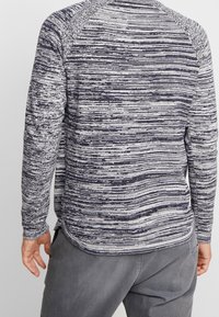 Chemise à manches longues avec un motif rayé texturé bleu marine et blanc, dotée d'un ourlet courbé et d'un col côtelé, fabriquée en tissu tricoté doux.