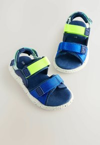 Blaue und grüne Sandalen mit verstellbaren Klettverschlüssen, gesprenkelter weißer Laufsohle und weichem Stofffutter. Offenes Zehendesign für Atmungsaktivität.