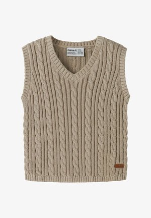 Gilet en tricot beige avec un col en V, présentant un motif en câble et une étiquette marron en bas à droite. Modèle sans manches, bords côtelés.