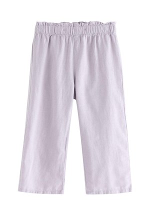 Smilende barn med krøllet hår iført hvid øjelygert top uden ærmer, lys lilla bukser med vide ben og hvide sko, stående på ensfarvet baggrund.