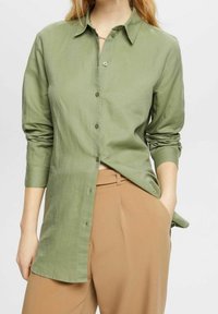 Camicia verde a maniche lunghe con colletto, realizzata in tessuto leggero, con chiusura a bottoni davanti e maniche arrotolate.
