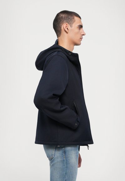 Navy hooded jacket with a zip front and side pockets, featuring a smooth texture and a slightly loose fit, styled with blue jeans.