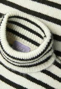 Pull enrayé noir et crème avec un col haut à côtes et une texture douce. L'étiquette indique "JJXX." Des peluches sont visibles sur la surface du tissu.