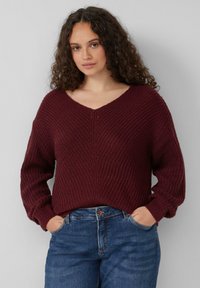 Bordeaux gebreide trui met een V-hals, verlaagde schouders, gestructureerde ribbels en een ontspannen pasvorm, gecombineerd met lichtblauwe denim jeans.