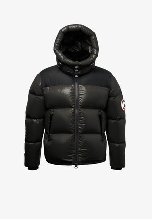 Czarna pikowana kurtka z wysokim kołnierzem z kapturem, błyszcząca tkanina, zamek błyskawiczny z przodu, dwie boczne kieszenie oraz naszywka z logo na lewym rękawie.