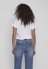 T-shirt en coton blanc avec les manches retroussées, associé à un jean en denim bleu taille haute doté de deux poches arrière et d'une finition délavée.