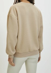 Felpa beige con vestibilità comoda, scollo rotondo e spalle scese. Presenta polsini e orlo a costine, realizzata in tessuto morbido.