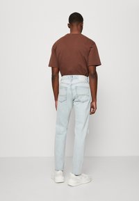 Brun kortärmad t-shirt och ljusblå jeans med rak passform, med bakfickor och ett vitt bälte, kombinerat med vita sneakers.