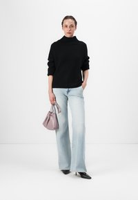 Pull à col roulé noir côtelé, jean flared bleu clair, petit sac à main lavande, escarpins noirs à bout pointu ; mannequin se tenant contre un fond blanc.