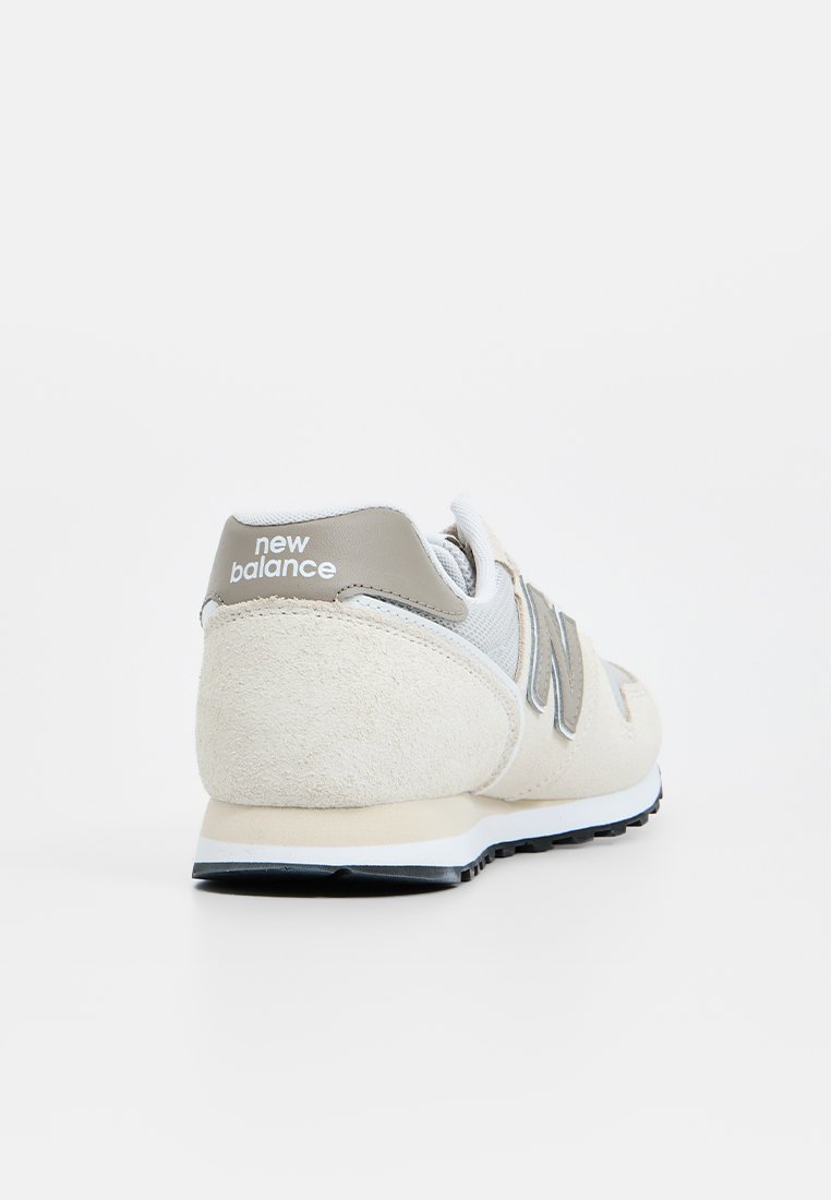 Baskets beiges et grises en cuir suédé et en maille, avec un col rembourré, un logo blanc et une semelle en caoutchouc noire. Vue arrière montrant les détails du design.