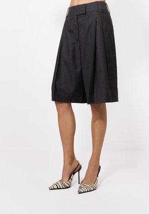 Kobieta ubrana w ciemnoszare plisowane spodenki sięgające kolan, połączone z czarno-białymi sandałami na obcasie w paski zebry z tylnym paskiem.