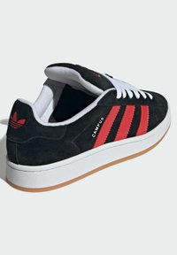 Scarpe da ginnastica in nabuk nero con strisce rosse, lacci bianchi e suola in gomma. Presentano un design piatto e un collarino imbottito per il massimo comfort.