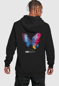 Hoodie noir avec un graphique coloré de papillon dans le dos, avec des teintes de bleu, de rose et de jaune. Texture douce avec une coupe décontractée.
