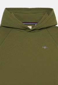 Felpa con cappuccio verde oliva, dotata di una tasca a marsupio frontale, maniche raglan e un piccolo logo ricamato sul petto. Tessuto di cotone morbido.