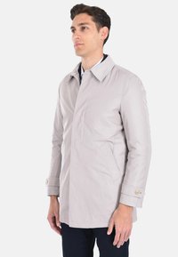 Cappotto grigio chiaro, resistente all'acqua, con collo a punta, due tasche laterali e polsini con bottoni. Tessuto liscio con una vestibilità dritta e sartoriale.