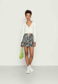 Camisola cropped de mangas compridas branca com detalhe de cordões, saia com padrão zebra preto e branco e mala verde. Ténis completam o visual.