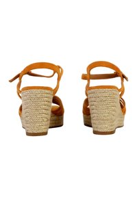 Brown wedge sandals with orange suede straps and a woven jute heel. Features a rounded shape and ankle ties for secure fit.