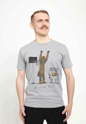 Gray cotton t-shirt featuring a cartoon of a character with fur and two figures in armor, with a basketball hoop and the text "Who invited him?"
