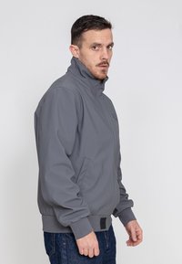 Graue, mit Reißverschluss versehene Jacke mit hohem Kragen, elastischen Bündchen und zwei Seitentaschen. Glattes Material mit minimalen Branding-Details.