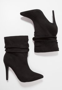 Bottines en suède noir avec un haut flou, un bout pointu et un fin talon haut. Texture lisse et design minimaliste.