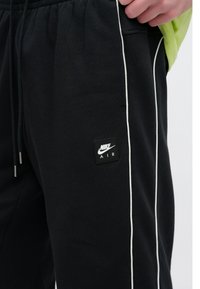 Μαύρο παντελόνι φόρμας Nike με λευκές πλευρικές ρίγες, ελαστική μέση και μαύρο σχέδιο με το λογότυπο Nike Air. Μαλακή υφή υφάσματος.