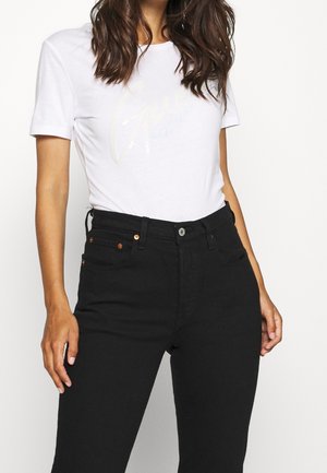 Hvid bomulds t-shirt med korte ærmer, der har et let grafisk print, samt højderede sorte jeans med kobberfarvet hardware og lommer.