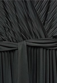 Robe noire plissée au design enveloppant, confectionnée dans un tissu doux et fluide, avec un détail de taille nouée, mettant en avant des plis sur l'ensemble.