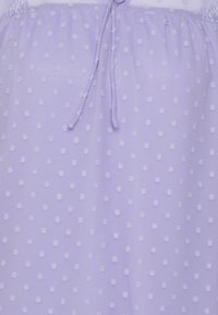 Tissu lilas avec des pois texturés, un design froncé et un détail de lien à œillets au niveau de l'encolure. Matériau doux et léger.