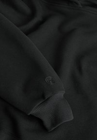 Sort sweatshirt med blød stoftekstur, ribbede manchetter og et lille præget logo på ærmet. Klassisk, afslappet design.